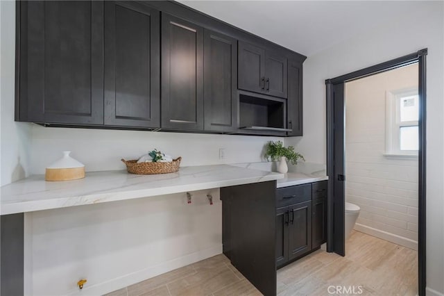kitchen featuring dark cabinets, light stone countertops, and light wood-type flooring