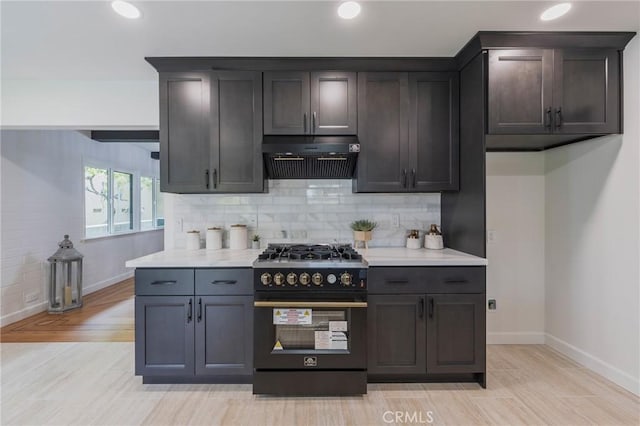 kitchen with range with gas cooktop, tasteful backsplash, light countertops, baseboards, and under cabinet range hood