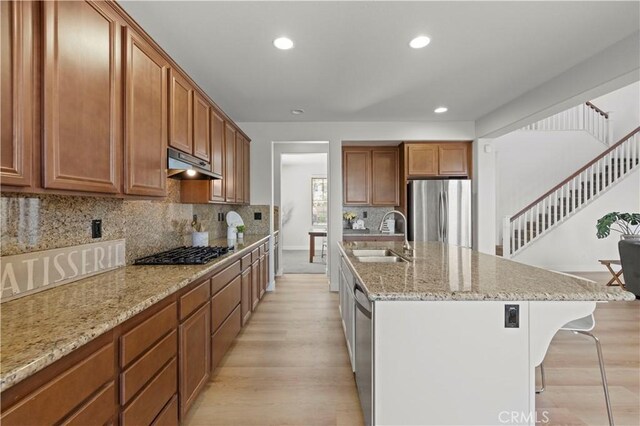 32177 Clear Springs Dr, Winchester, CA 92596 - kitchen with appliances with stainless steel finishes, under cabinet range hood, light wood-style flooring, a breakfast bar area, and brown cabinets