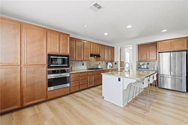 32177 Clear Springs Dr, Winchester, CA 92596 - kitchen with appliances with stainless steel finishes, brown cabinetry, a breakfast bar, light wood-type flooring, and recessed lighting