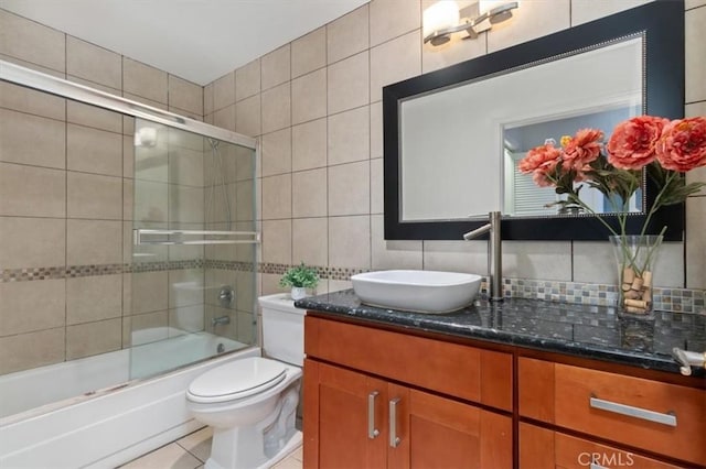 full bath with tile walls, decorative backsplash, vanity, shower / bath combination with glass door, and toilet