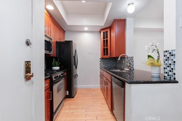 kitchen featuring stainless steel appliances, a sink, light wood-style flooring, decorative backsplash, and glass insert cabinets