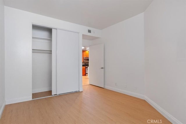 unfurnished bedroom featuring light wood finished floors, baseboards, and a closet