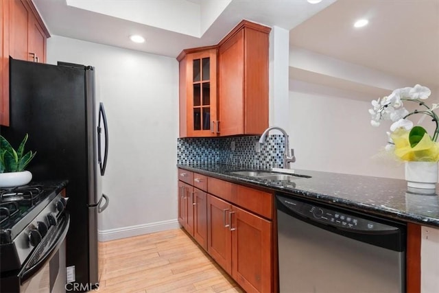 kitchen with stainless steel appliances, a sink, light wood-type flooring, dark stone countertops, and decorative backsplash