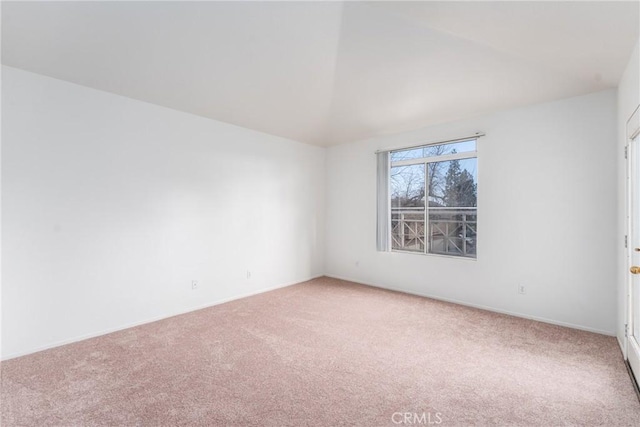 spare room featuring vaulted ceiling, light colored carpet, and baseboards