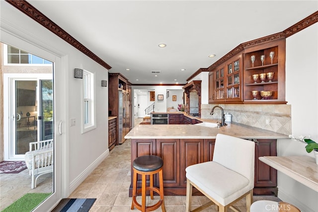 kitchen with glass insert cabinets, baseboards, a sink, a peninsula, and backsplash