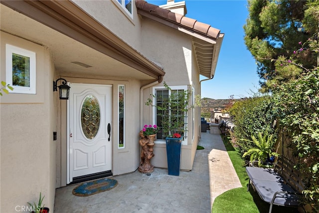 entrance to property with stucco siding, fence, and a patio