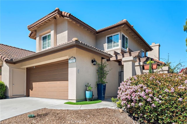 mediterranean / spanish house featuring stucco siding, a garage, a tiled roof, and driveway