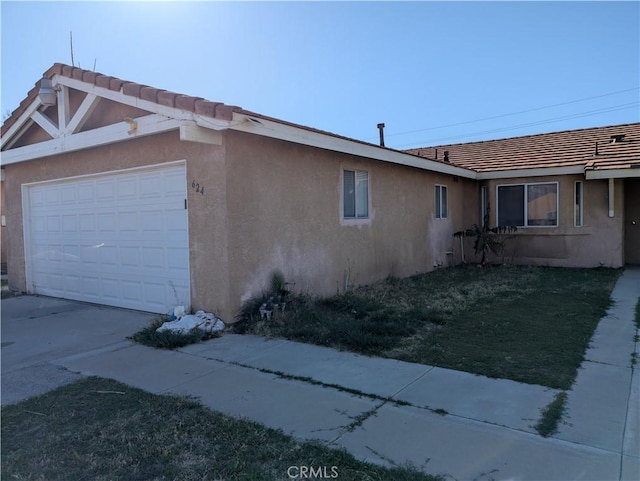 view of side of home with a garage, a tiled roof, driveway, and stucco siding