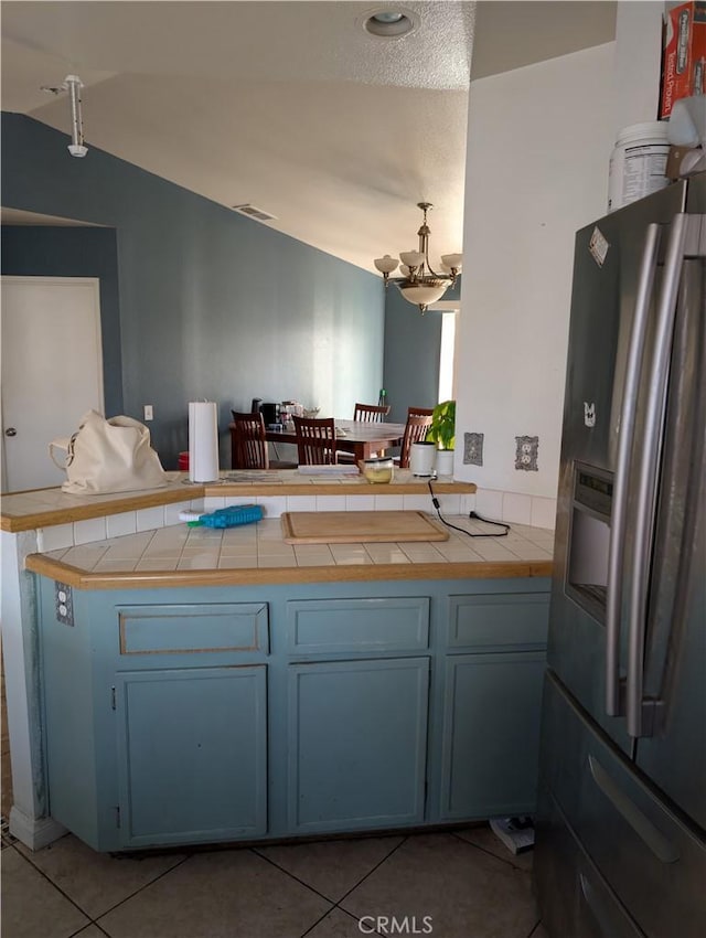 kitchen featuring lofted ceiling, an inviting chandelier, tile countertops, light tile patterned floors, and stainless steel fridge