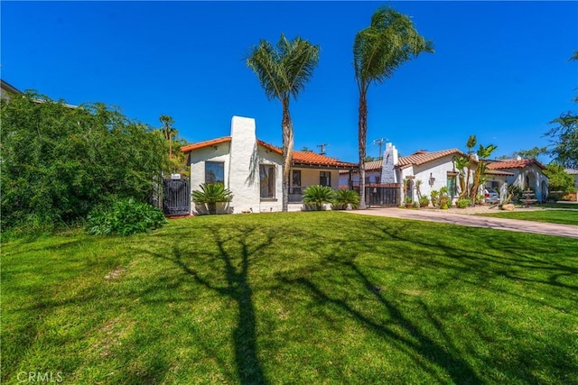 mediterranean / spanish home with stucco siding, a front yard, a gate, a chimney, and driveway