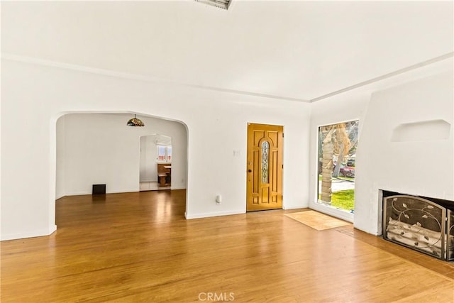 unfurnished living room with arched walkways, a fireplace, baseboards, and wood finished floors