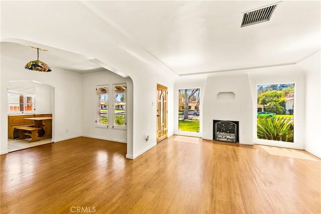 unfurnished living room featuring arched walkways, a fireplace with flush hearth, visible vents, and wood finished floors