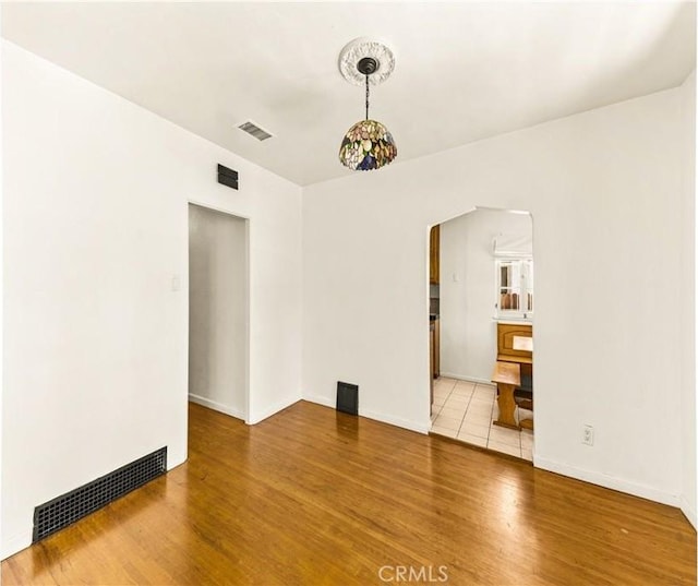 empty room with visible vents, baseboards, arched walkways, and wood finished floors