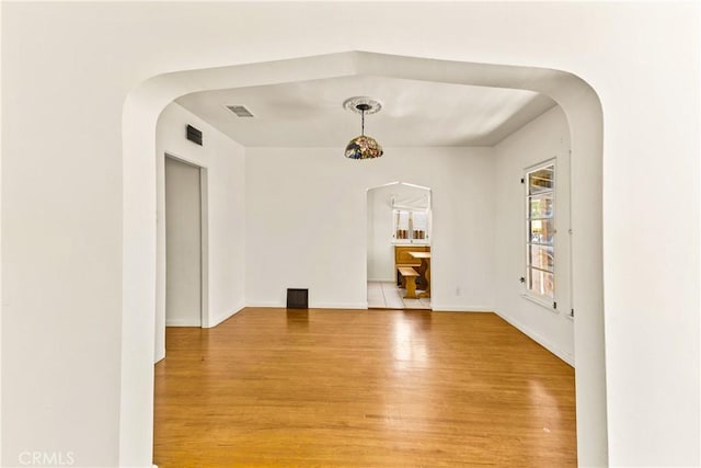 unfurnished room with arched walkways, baseboards, visible vents, and light wood-type flooring
