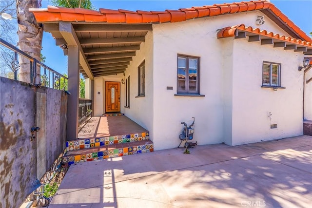 exterior space with stucco siding, fence, and a tile roof