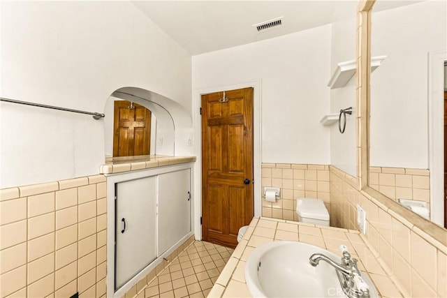 bathroom featuring tile patterned floors, toilet, visible vents, tile walls, and a sink