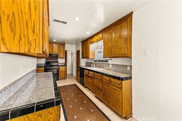 kitchen with visible vents, black appliances, light tile patterned flooring, a sink, and brown cabinets