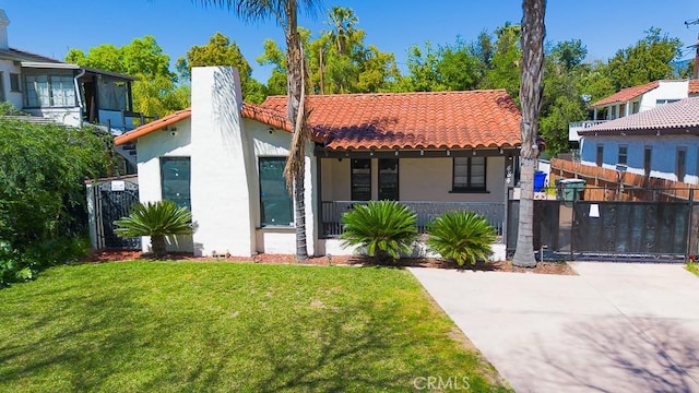 mediterranean / spanish home featuring stucco siding, a front yard, a tiled roof, fence, and covered porch