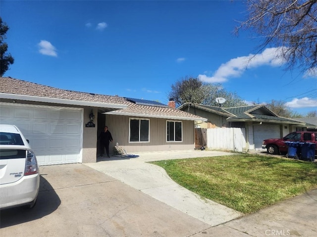 ranch-style home featuring fence, an attached garage, driveway, a front yard, and solar panels