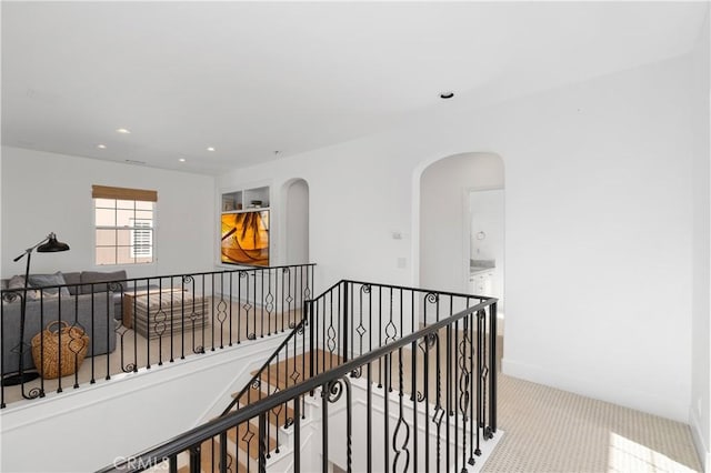 corridor featuring arched walkways, recessed lighting, and an upstairs landing