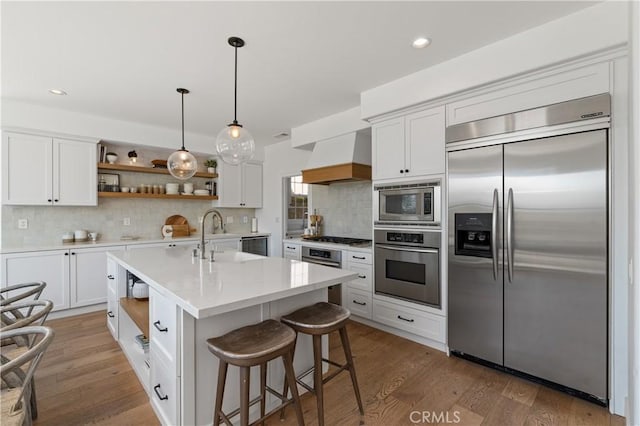 kitchen featuring built in appliances, premium range hood, a sink, and open shelves