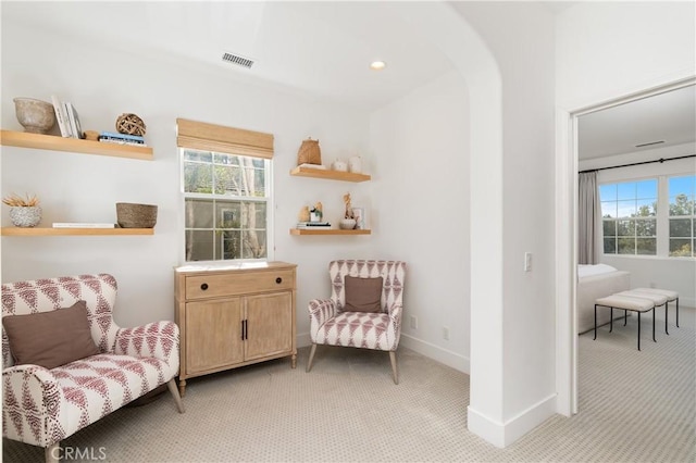 living area featuring visible vents, light carpet, baseboards, and arched walkways