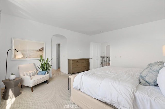 bedroom featuring arched walkways and light colored carpet