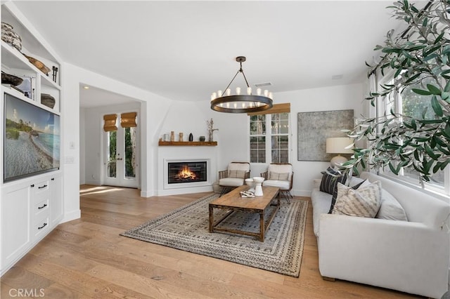 living area featuring a notable chandelier, baseboards, visible vents, and wood finished floors