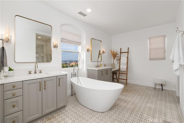 full bath with visible vents, a freestanding tub, a sink, a shower, and two vanities