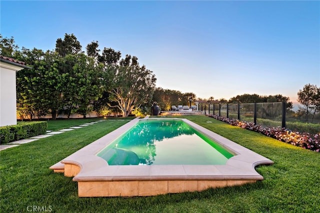 pool at dusk featuring a yard and a fenced backyard