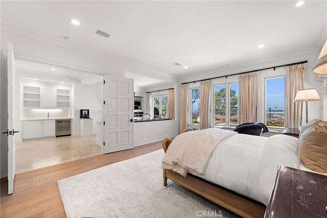 bedroom featuring ornamental molding, bar area, recessed lighting, light wood-style flooring, and beverage cooler