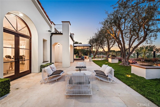 patio terrace at dusk featuring a balcony, french doors, and a lawn