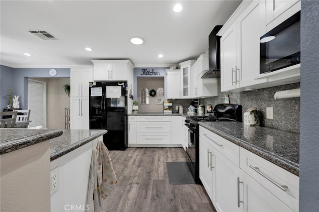 kitchen featuring wood finished floors, visible vents, wall chimney range hood, black appliances, and white cabinetry