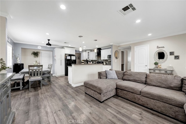 living area with wood finished floors, visible vents, recessed lighting, and crown molding