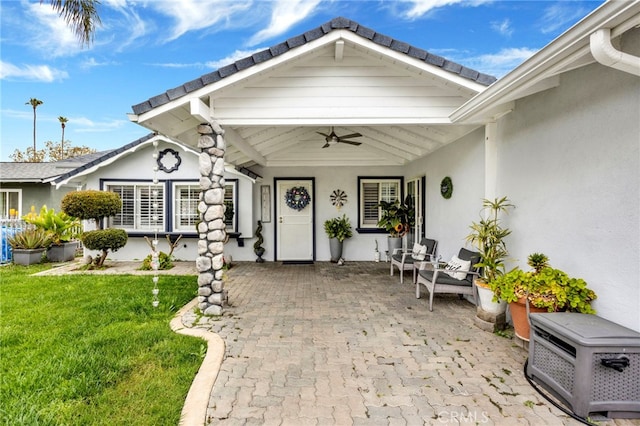 doorway to property with a yard, a ceiling fan, a patio area, and stucco siding