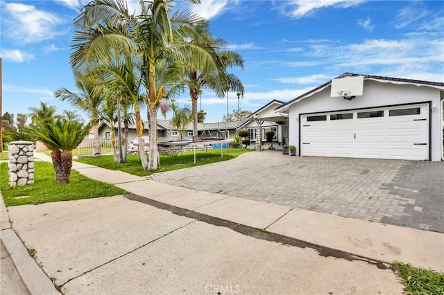 ranch-style home with fence, a garage, a front yard, stucco siding, and decorative driveway