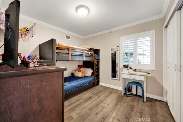 bedroom with baseboards, wood finished floors, visible vents, and ornamental molding