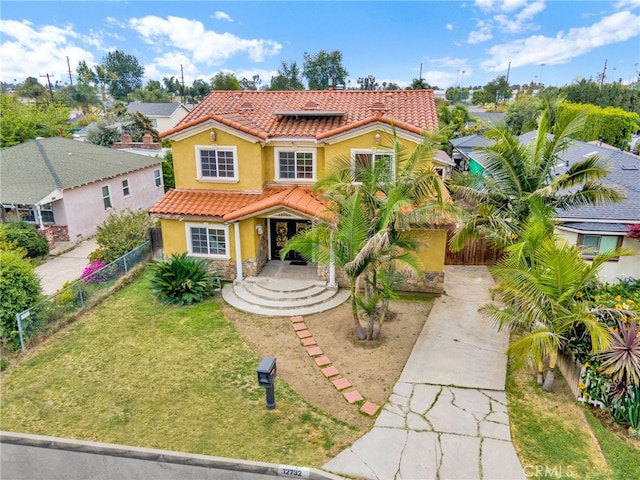 mediterranean / spanish-style home featuring a front lawn, a tiled roof, driveway, stone siding, and fence