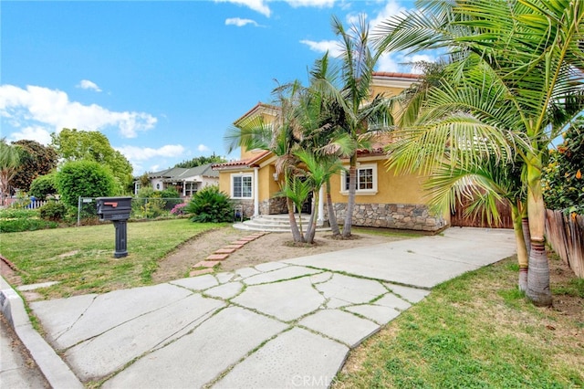 mediterranean / spanish-style house featuring a front lawn, driveway, stone siding, fence, and stucco siding