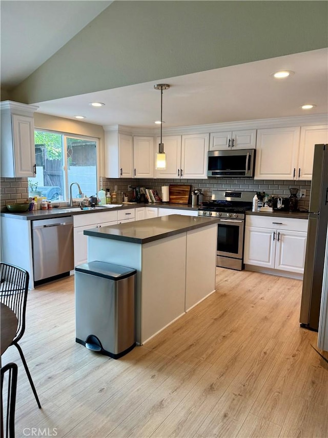 kitchen with white cabinets, stainless steel appliances, dark countertops, light wood-type flooring, and vaulted ceiling