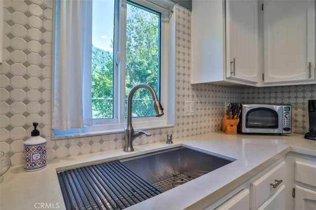 kitchen with stainless steel microwave, tasteful backsplash, light countertops, white cabinetry, and a sink