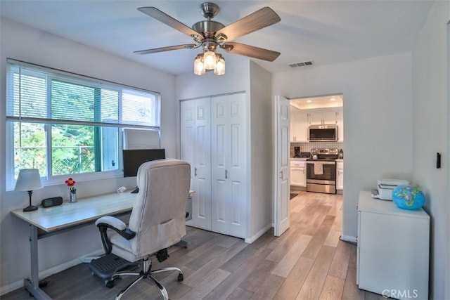 office area with light wood-style floors, baseboards, a ceiling fan, and visible vents