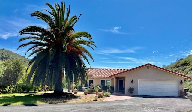 view of front of house featuring a tiled roof, a garage, stucco siding, and aphalt driveway