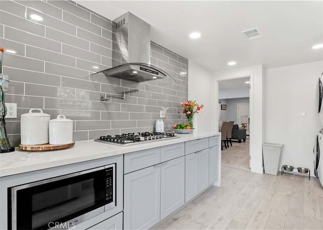 13118 Hoyt St, Pacoima, CA 91331 - kitchen featuring light wood-type flooring, decorative backsplash, visible vents, wall chimney range hood, and appliances with stainless steel finishes