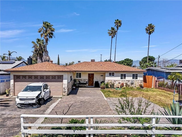 single story home with a fenced front yard, an attached garage, stone siding, aphalt driveway, and stucco siding