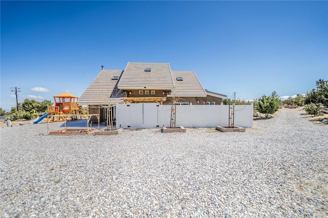rear view of property featuring fence, stucco siding, a tiled roof, and a playground