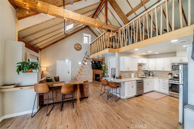 kitchen featuring open floor plan, white cabinets, a kitchen bar, appliances with stainless steel finishes, and light wood finished floors
