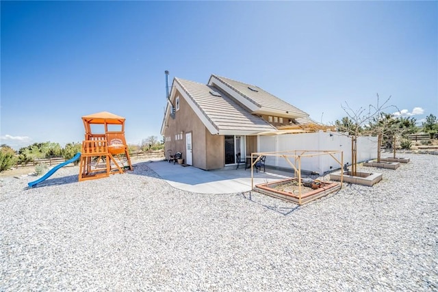 back of house featuring a patio, stucco siding, a tile roof, a playground, and a vegetable garden