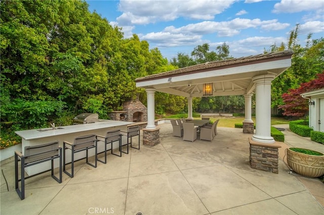 view of patio with an outdoor stone fireplace, outdoor dry bar, area for grilling, outdoor dining area, and a gazebo